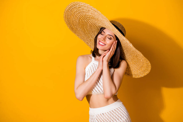 Photo of shiny adorable lady wear white outfit hat arms hands cheek cheekbone closed eyes isolated yellow color background. - Фото, изображение