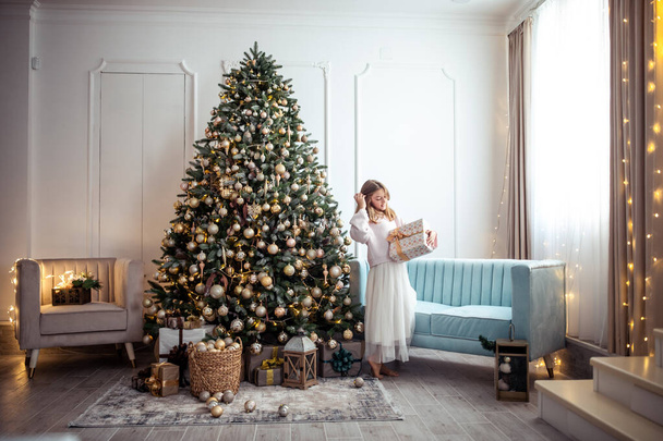 Schattig tienermeisje in een kamer met een versierde kerstboom. De wintervakantie. Hoge kwaliteit foto - Foto, afbeelding
