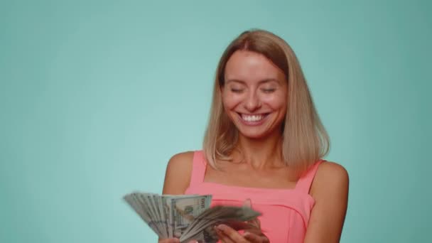 Rich pleased boss blonde woman waving money dollar cash banknotes bills like a fan, success business career, lottery winner, big income, wealth. Young girl isolated alone on blue studio background - Footage, Video