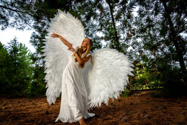 Egy gyönyörű szőke modell pózol a szabadban, miközben fehér szárnyakat visel Halloweenkor..  - Fotó, kép