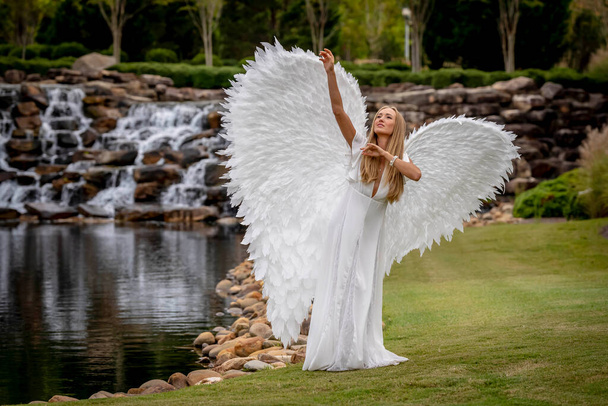 Egy gyönyörű szőke modell pózol a szabadban, miközben fehér szárnyakat visel Halloweenkor..  - Fotó, kép