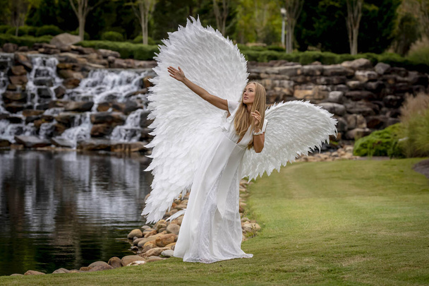 Una hermosa modelo rubia posa al aire libre mientras usa un conjunto de alas blancas para Halloween.  - Foto, imagen