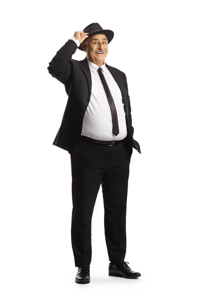 Elegant mature man in black suit and tie greeting with a fedora hat isolated on white background - Photo, image