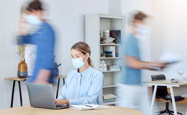 Bizneswoman, zajęty biuro i covid zgodności podczas gdy na laptopie i rozmycia ludzi wokół niej. Pracownicy w biurze podczas koronawirusu noszący maskę i pracujący w firmie po zamknięciu. - Zdjęcie, obraz