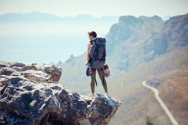 Retkeilijä, seikkailu ja vuoren huipulla nainen kalliokiipeily, näkymä ja reppu luonnossa. Aktiivinen naispuolinen matkustaja vaellus- tai vaellusmatkalla seisoo kalliolla kauniilla näköalalla ulkona. - Valokuva, kuva