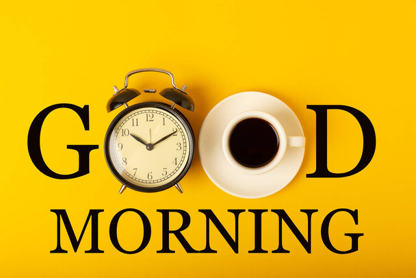 Heißer Kaffee in einer weißen Kaffeetasse auf gelbem Hintergrund mit der Aufschrift "GUT MORNING". Konzeptfoto.Design.Heißgetränkekonzept.Kopierraum.Aufsicht.Platz für Text. - Foto, Bild
