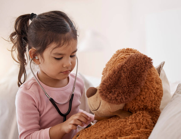 Stethoscope, girl and a teddy bear playing future doctor game showing care on a good health insurance checkup. Cute small child listening or checking stuffed animal medical heartbeat at home. - Fotografie, Obrázek