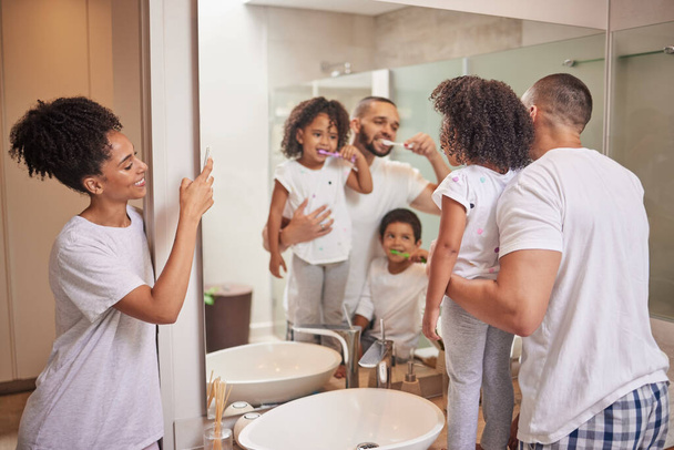 Vater bringt Kindern bei, im Badezimmer Zähne zu putzen, glückliche Mama fotografiert Kinder lernen Zahngesundheit und morgens in der Mami-Wohnung. Eltern reinigen Mund, Körperpflege und Foto des Familienspiegels. - Foto, Bild