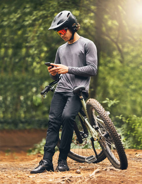 Fitness, forest and phone with man and bike relax with internet, social media or online in nature. Wellness, mountain and sports with athlete on adventure, exercise or peace training on park trail. - Photo, image