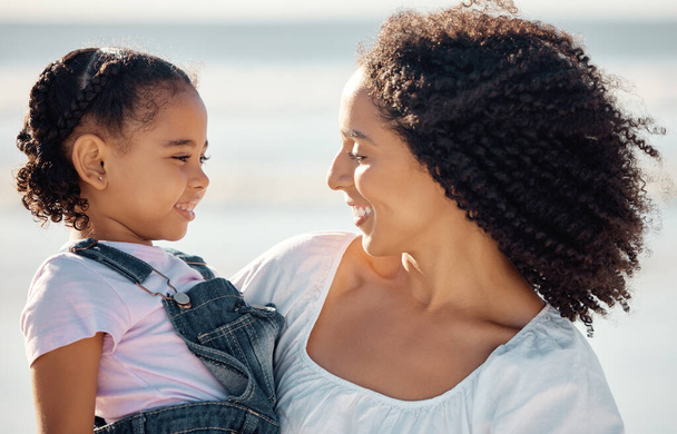 Mom with child at beach smile, make eye contact and black family happiness. Black woman with girl, happy spend time as mother and daughter, on family holiday or vacation by the ocean in Brazil. - Photo, Image