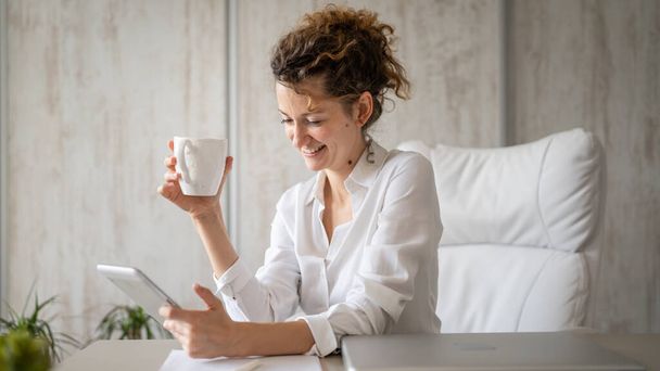 Genç bir iş kadını Kafkasyalı kadın dijital tablet kullanarak ofise geri dönüyor ve kahve girişimcisi modern iş konseptini içiyor. - Fotoğraf, Görsel