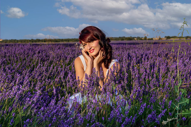 Woman looking at camera and smiling while posing outdoors in a lavender flower field. Nature concept. - Zdjęcie, obraz