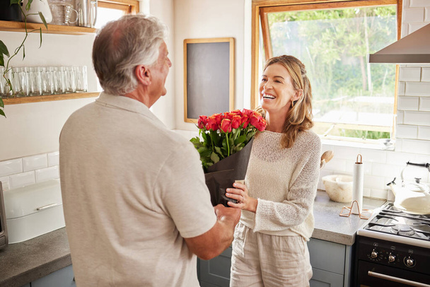 Surprise flowers, love celebration and couple with smile to celebrate birthday, anniversary or romantic event in home kitchen. Senior man and woman giving bouquet of roses as present or gift. - Photo, image