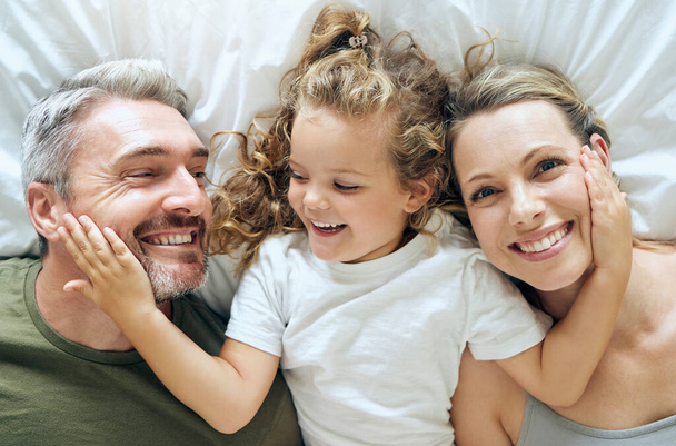Perhe, onnellinen ja hymy ihmisiä ylhäältä sängyssä kotona rentoutua makuuhuoneessa. Äiti, tyttö ja mies onnellisina yhdessä talossa rakkaudella, huolenpidolla ja rauhallisella hymyllä positiivisella ajattelutavalla. - Valokuva, kuva