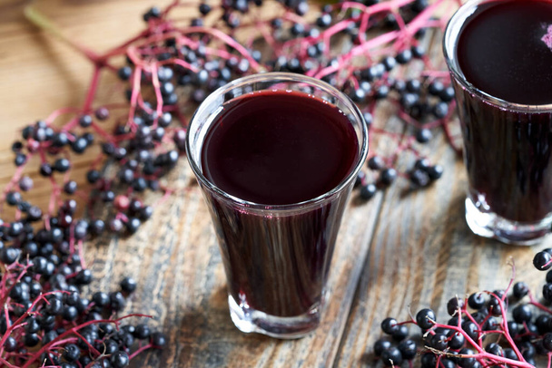 Homemade black elder syrup with fresh elderberries on a wooden table - Photo, image