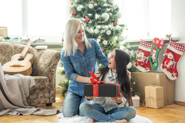 Veselé Vánoce a veselé svátky. Veselá matka a její roztomilá dcera si vyměňují dárky. Máma a malý dítě se baví doma u stromu. Milující rodina s dárky na pokoji. - Fotografie, Obrázek