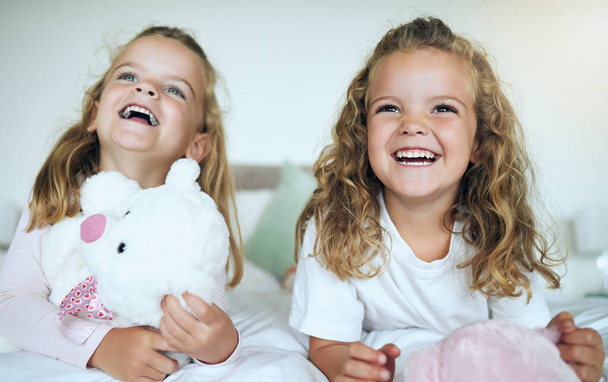 Children, teddy bear and happy sisters playing together in their bedroom at their family home. Happiness, smile and bond between twin siblings holding a toy while relaxing on a bed in their room - Foto, Imagen