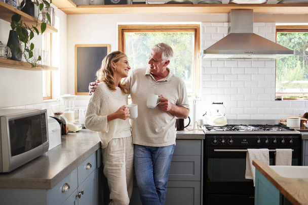 Senior, couple and drinking coffee with a love, marriage and happiness morning mindset at home. Happy smile and hug of a elderly woman and man with tea in a house kitchen together with quality time. - Фото, изображение