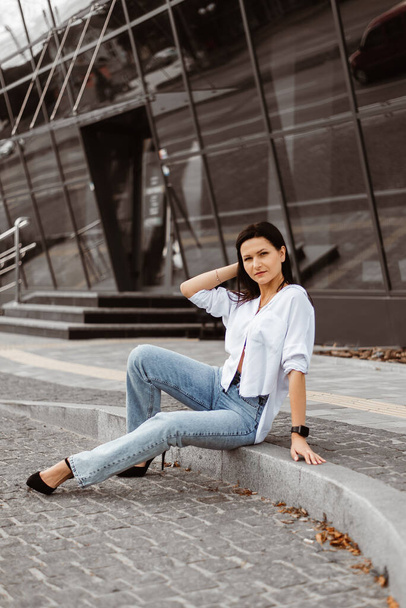 Une jeune femme pose dehors en jeans et un chemisier blanc - Photo, image