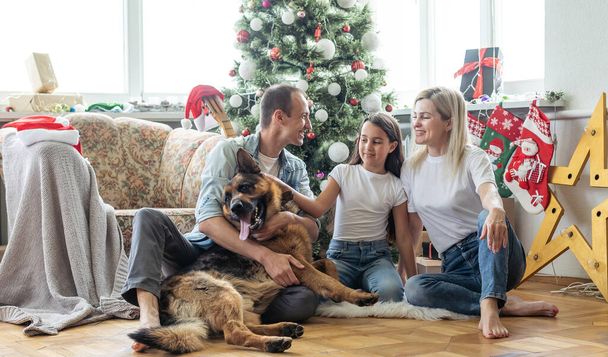 família sorridente e filha com cão sentado perto da árvore de natal com presentes. - Foto, Imagem
