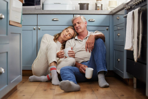 Seniorenpaar, Liebe und Unterstützung beim Zusammensitzen und sich sicher fühlen, entspannen und in Ruhe Kaffee trinken und gemütlich auf dem Küchenboden kleben. Glücklicher alter Mann und Frau genießen gemeinsam den Ruhestand. - Foto, Bild