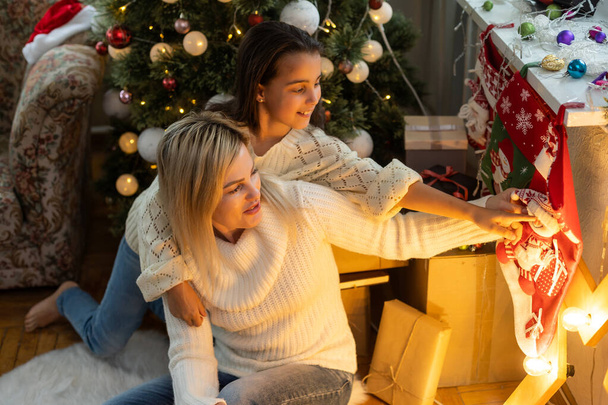 Äiti ja tytär joulukuusen edessä, avaamalla lahjoja
. - Valokuva, kuva