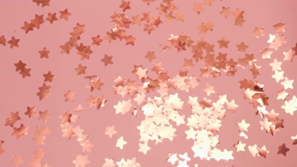 Gouden ballonnen in de vorm van vier valt op roze vloer met verspreide sterren van confetti cracker. Viering van de verjaardag in roze studio closeup. - Video