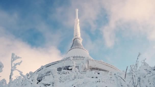 Giant Spire του πύργου Jested σε ομίχλη κατά του μπλε ουρανού με αιωρούμενα σύννεφα. Κατεψυγμένα δέντρα αναπτύσσονται στο βουνό κοντά φουτουριστική κατασκευή το χειμώνα χαμηλή γωνία shot - Πλάνα, βίντεο