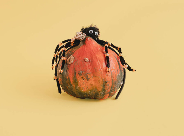 Dynia i sztuczny pająk na żółtym tle. Minimalna kompozycja pozioma, zabawna koncepcja Halloween - Zdjęcie, obraz