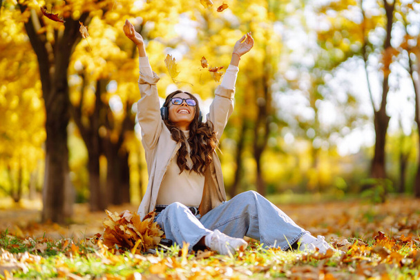 Young  woman smiling and throwing maple leaves up in the air. - Foto, Imagem