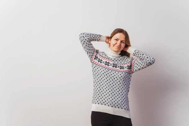 Russian girl in a knitted pullover on a white wall. Slav girl in a Turkish knitted New Year's sweater on a light wall. Christmas sweater with stars on a woman for a photo shoot - Photo, Image