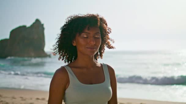 Peaceful woman meditating beach with serene smile on face close up. Calm girl putting hand on chest feeling peace harmony with nature. African american lady closing eyes relax on seashore at sunrise. - Footage, Video
