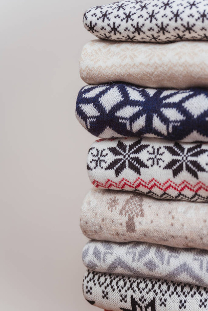 Az újévi meleg kötött pulóverek egymás mellett fekszenek. kötött karácsonyi pulóver, fehér alapon összehajtogatott mintával.kötött karácsonyi pulóver textúrája - Fotó, kép