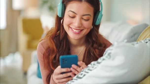 Girl, phone and music on sofa to relax with headphones with smile, typing and happy on social media. Woman, smartphone and streaming song on internet while reading communication, blog post or email. - Footage, Video