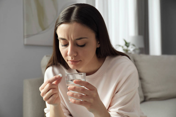 Young woman with abortion pill and water indoors - Foto, Imagem