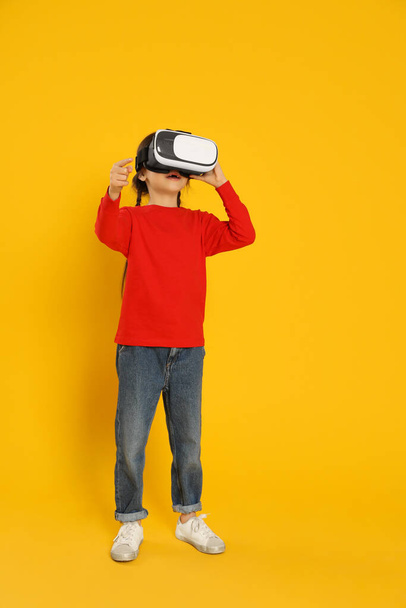Little girl using virtual reality headset on yellow background - Foto, Imagem