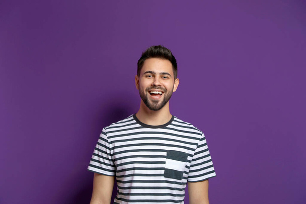 Young man laughing on purple background. Funny joke - 写真・画像