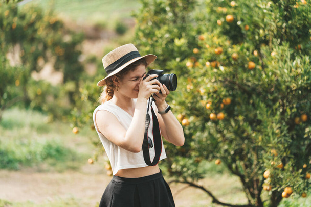 A woman in a straw hat is making pictures in an orange garden. High quality photo - Foto, imagen
