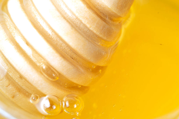 Honey drips from a wooden honey dipper on a yellow background. Sweet bee product for your design with copyspace. Close-up - Photo, Image
