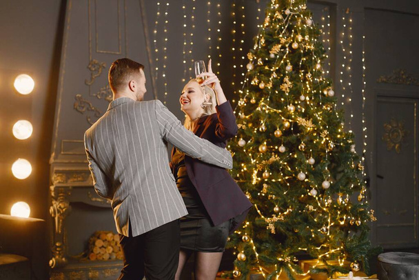Romantic couple dancing in decorated living room by christmas tree. Couple celebrating new year party. Man wearing elegant costume and woman black dress. - Valokuva, kuva