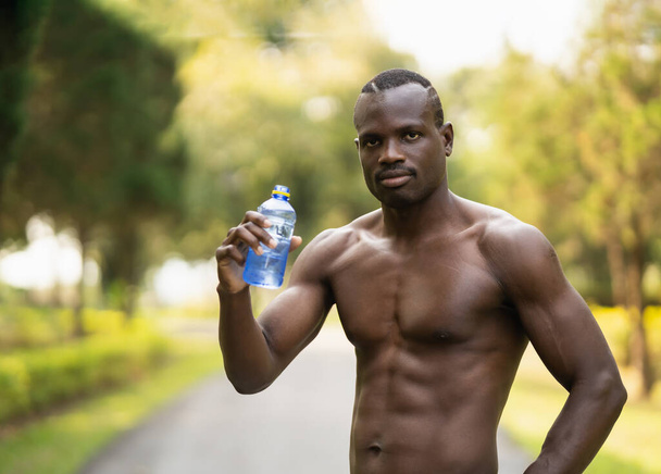 Ελκυστικός άνθρωπος του αφρικανικού αθλητισμού κουρασμένος και διψασμένος μετά από τρέξιμο προπόνηση πόσιμο νερό.Αθλητές Αφρικανός άνθρωπος ξεκουράζεται μετά την προπόνηση τρέχει στο πάρκο κήπο. Αθλητικός άνθρωπος έννοια. - Φωτογραφία, εικόνα