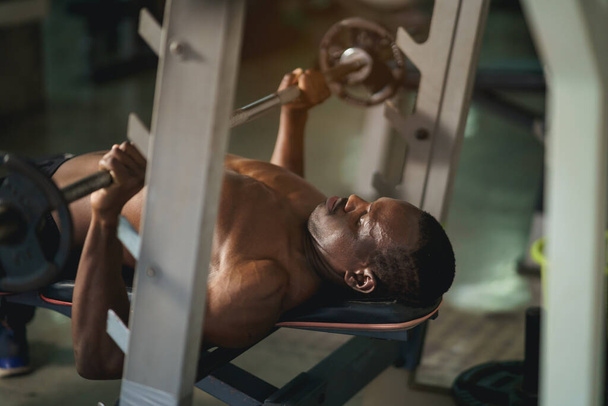 Hombre de deporte africano músculo fuerte ejercitar en pesas con mancuerna para el entrenamiento en el pecho en la sala de fitness en el gimnasio. Culturismo deporte hombre fitness concepto. - Foto, imagen