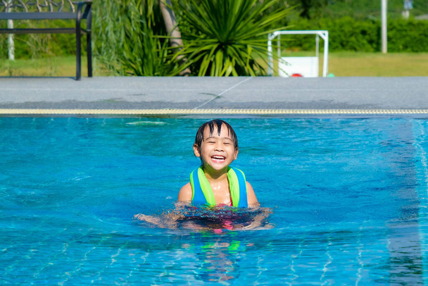 La bambina gioca nella piscina all'aperto del resort tropicale durante le vacanze estive in famiglia. Bambini che imparano a nuotare. Attività estive salutari per bambini. - Foto, immagini