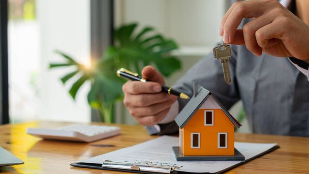 Der Immobilienmakler hält die Hausschlüssel nach Vertragsunterzeichnung an den Kunden. Verkaufsideen für Immobilien - Foto, Bild