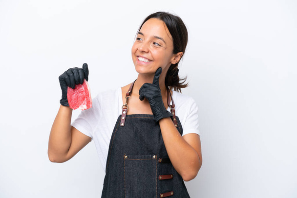 Butcher hispanic woman wearing an apron and serving fresh cut meat isolated on white background thinking an idea while looking up - Foto, afbeelding