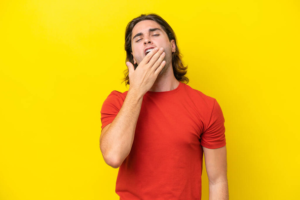 Кавказький красивий чоловік ізольований жовтим фоном позіхаючи і покриваючи широкі відкриті рот рукою. - Фото, зображення