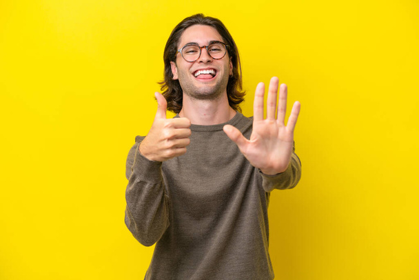 Caucasiano bonito homem isolado no fundo amarelo contando seis com os dedos - Foto, Imagem