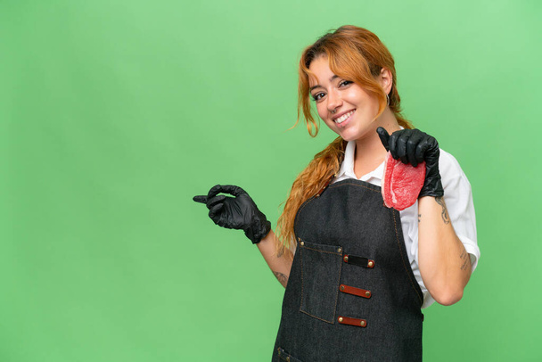 М'ясник біла жінка в фартусі і подає свіже нарізане м'ясо ізольоване на зеленому екрані ключовий фон хроми, спрямований палець на бік
 - Фото, зображення