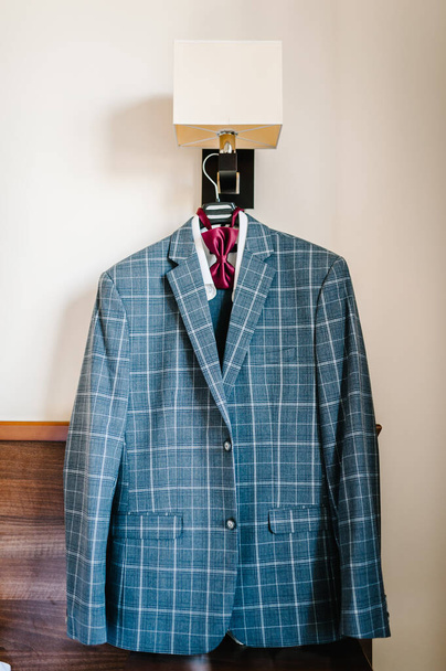 A man's jacket, blue suit with bow-tie on a hanger in the room. Stylish blue wedding. - Фото, изображение