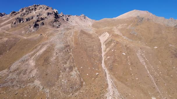 Drone vista de las montañas de piedra con acantilados empinados. Otoño en las montañas. Las colinas están cubiertas de hierbas amarillas y arbustos. El cielo es azul, el sol brilla intensamente. Kazajstán - Imágenes, Vídeo